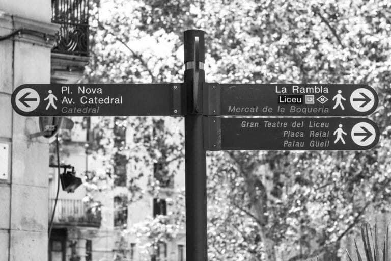 A street sing post with arrows pointing to different locations in Barcelona.