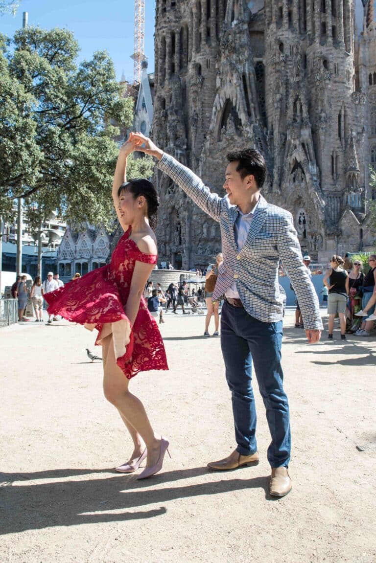 A couple in front of the Sagrada Familia, she is being spun around while walking with him in the park.
