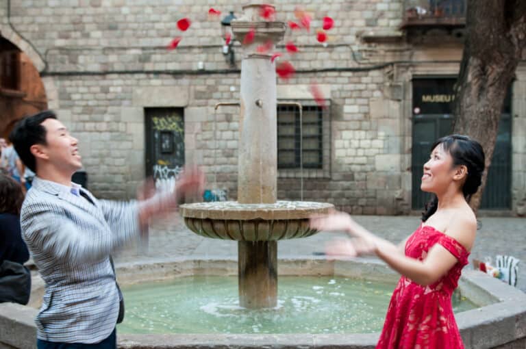 A couple during an engagement photo shoot in the gothic quarter throwing rose petals into the air.